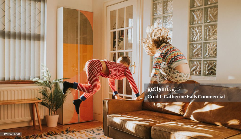 Children Bouncing on a Brown Leather Sofa in a Sunny Domestic Room