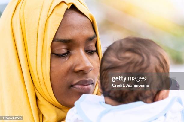 muslim mother holding her baby - african refugee stock pictures, royalty-free photos & images