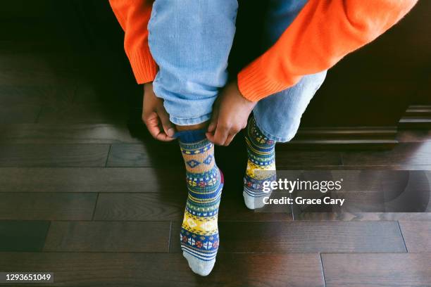 woman puts on colorful wool socks with light blue jeans - cropped trousers stock-fotos und bilder