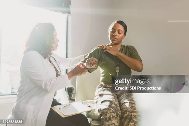 female veteran discusses shoulder pain with doctor - injured soldier imagens e fotografias de stock