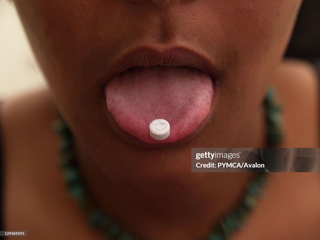 Girl with an ecstasy tablet on her tongue, smiley faced pill, UK 2004