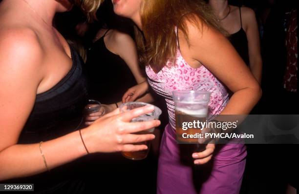 Two girls, drinking pints of lager, dancing and smiling, UK 2004