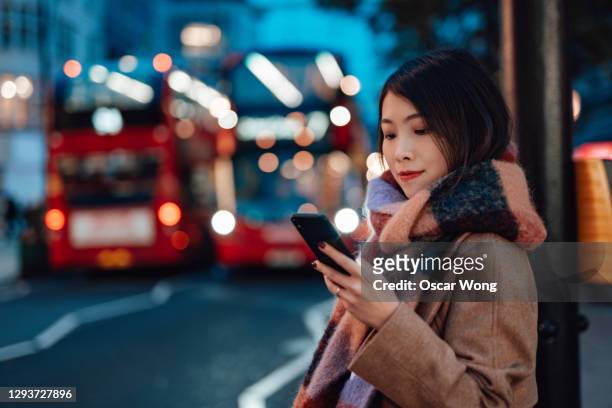 young woman arranging taxi service with smartphone on the city street at night - bus road stock pictures, royalty-free photos & images
