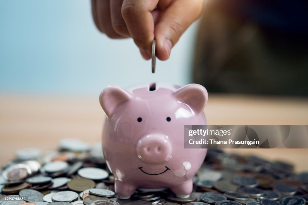 Person Putting Coin In Piggy Bank At Table