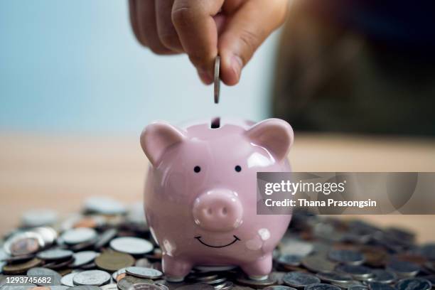 person putting coin in piggy bank at table - saving imagens e fotografias de stock