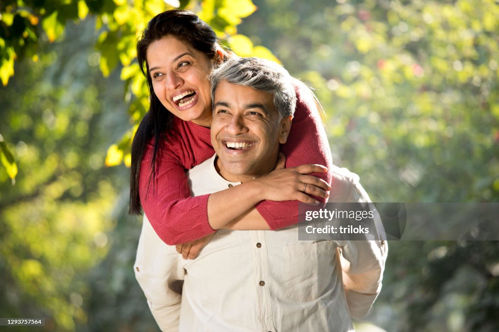 Man piggybacking his wife at park