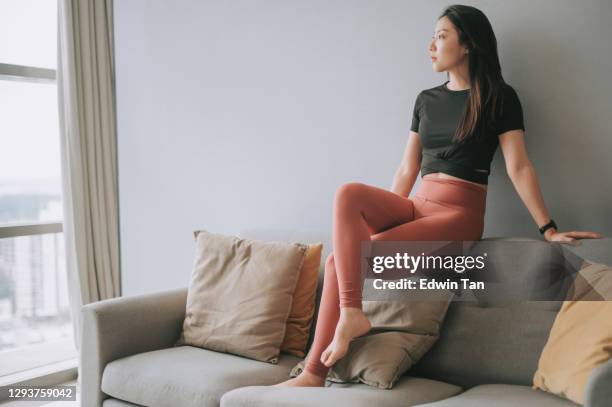 asiatische chinesische schöne frau mit yoga-kleidung sitzt auf sofa posiert im wohnzimmer - legging stock-fotos und bilder