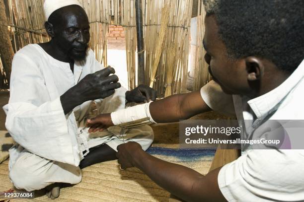 Witch doctor using strips of material and stick splints to bandage patient with broken wrist, While traditional medicine still holds sway in Sudan, a...