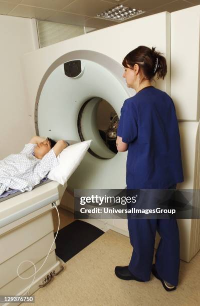 Patient on examination table of computed tomography scanner assisted by nurse