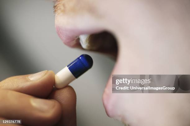 Close-up of young man placing blue and white tablet into mouth