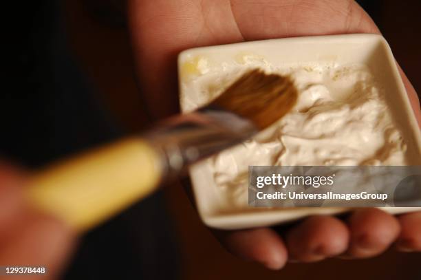The hands of a beautician holding a dish of facial powders. , The powders will be mixed with oils to create a facemask, to be applied to the face of...