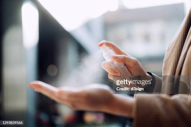 close up of young asian woman sanitizing her hand with disinfectant spray outdoors in the city against sunlight, with urban city buildings in background - desinfetar imagens e fotografias de stock