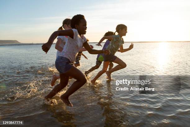 children running and splashing in the sea at sunset - race unity stock pictures, royalty-free photos & images