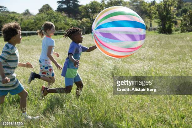 children playing with inflatable ball in a field - children only stock pictures, royalty-free photos & images