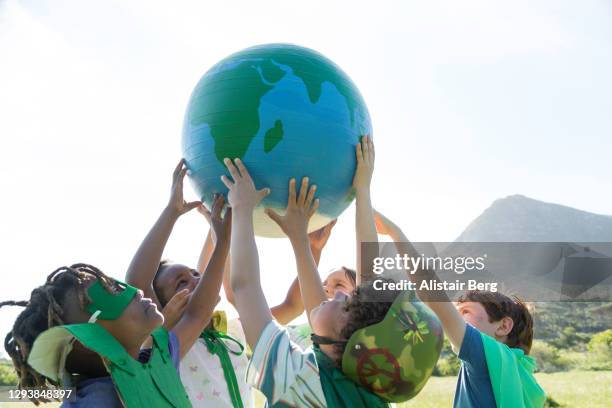 group of children holding up a large globe - globe stockfoto's en -beelden