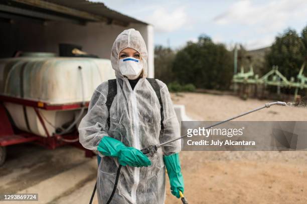 woman with the fumigation suit to apply pesticides to cultives. woman dressed in phytosanitary suit and mask poses with tank for spraying or disinfectant in the background.fumigation, agriculture. - farmer fertilizer stock pictures, royalty-free photos & images