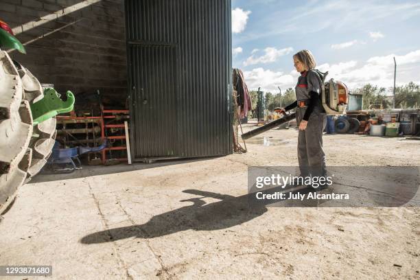 woman with a blower cleans the interior of an agricultural material storage warehouse. blowing machine backpack cleaning tractor. - leaf blower stock pictures, royalty-free photos & images