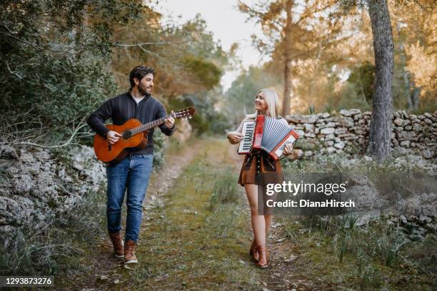 beautiful young couple playing music together while walking in the nature with the guitar and accordion - accordionist stock pictures, royalty-free photos & images