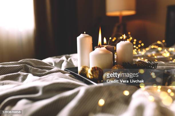 candles on the bed focus. cosy bedroom interior with bed, plaids, flashlights, candles and dark walls. christmas decoration. white bedding sheets with striped blanket and pillow. hygge concept. - christmas candles stockfoto's en -beelden