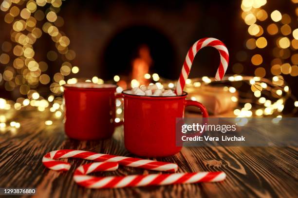 hot drink with marshmallows and candy cane in red mug. fir cones, spices, fireplace, box of gifts in the background. cozy seasonal holidays - candy cane stock pictures, royalty-free photos & images
