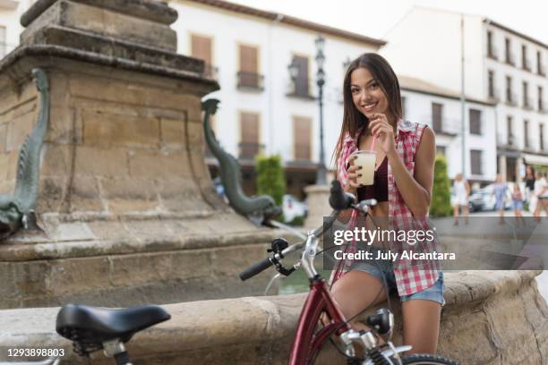 a pretty and young woman smiles eats lemon slush on a summer day with her bike parked - frozen drink stock pictures, royalty-free photos & images