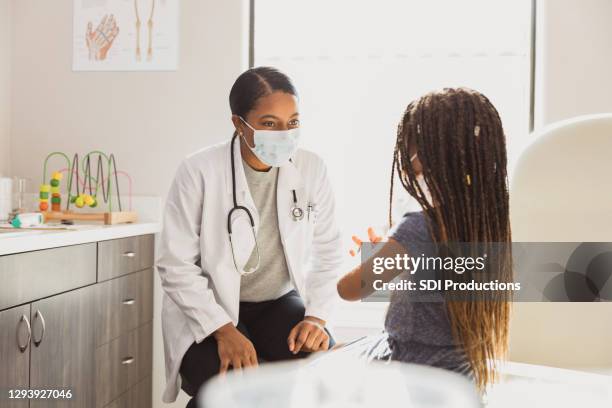 pediatrician smiles through protective mask as young patient speaks - female doctor with mask stock pictures, royalty-free photos & images