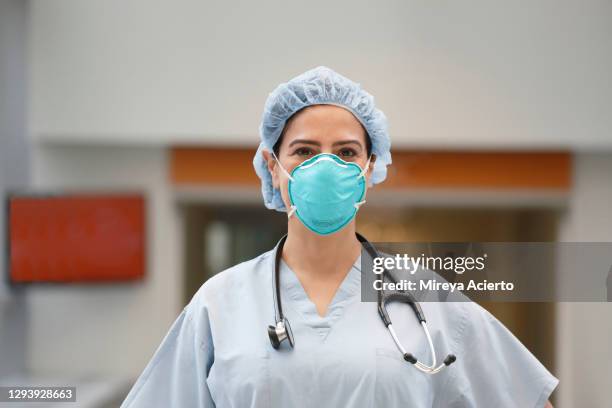 portrait of a middle eastern female health care provider wearing light green medical scrub, a stethoscope and an n95 protective face mask in a brightly lit hallway. - mascarilla-n95 fotografías e imágenes de stock