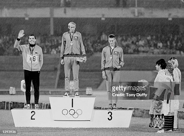 David Hemery of Great Britain stands on the first place podium flanked by Gerhard Hennige of Germany and John Sherwood of Great Britain during the...