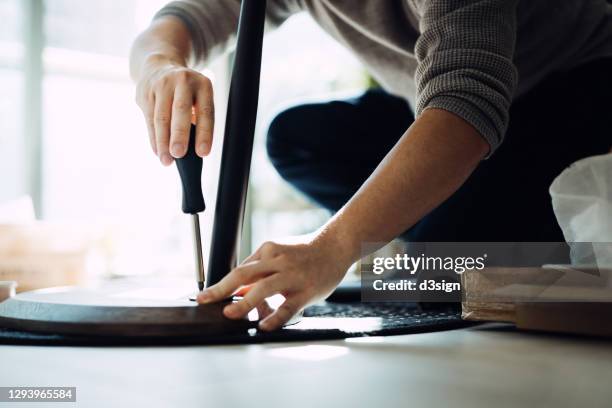 close up of young asian man assembling furniture with a screwdriver, he is setting up a wooden coffee table in newly refurbished apartment against sunlight - destornillador fotografías e imágenes de stock