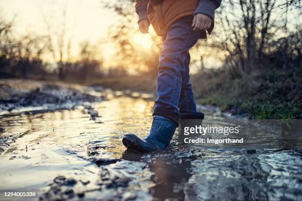 bambino che cammina nella pozzanghera fangosa il giorno d'inverno. - wellington boot foto e immagini stock