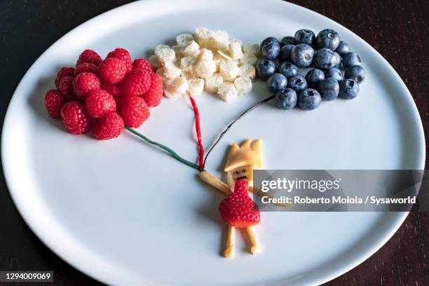 fruit creation of child holding balloons of berries in white plate - gobernador fotografías e imágenes de stock