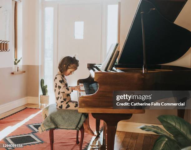 little girl playing a grand piano in a domestic environment - child pianist stock pictures, royalty-free photos & images