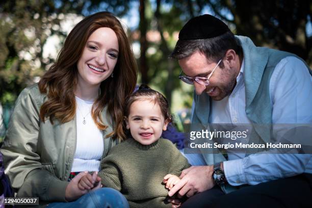 a young jewish family sitting on a park bench and posing for the camera - calotte photos et images de collection