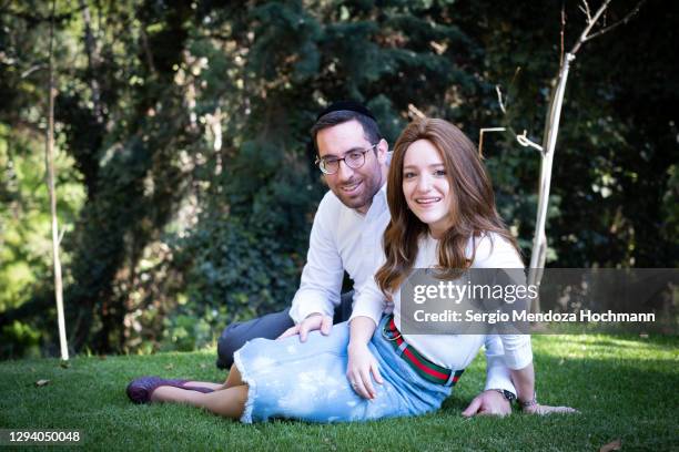 a young jewish couple sitting on the grass in a public park looking at the camera - orthodox jodendom stockfoto's en -beelden