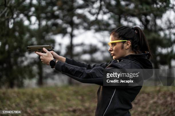 mujer joven apuntando y practicando disparos desde la pistola en el campo de tiro - self defense fotografías e imágenes de stock