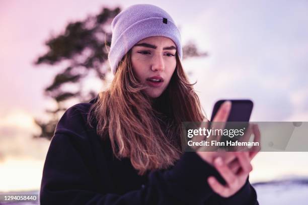 teenage girl reading bad news on mobile phone outdoors in winter landscape - cell phone confused stock pictures, royalty-free photos & images