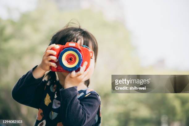 niña asiática jugando con la cámara de juguete en el parque - photographing fotografías e imágenes de stock