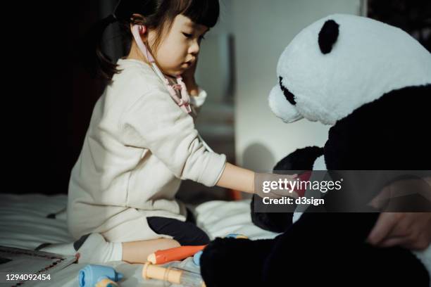 adorable little asian girl playing a doctor game with her beloved soft panda toy, listening the heartbeat of the soft panda toy with a stethoscope at home - acteren stockfoto's en -beelden