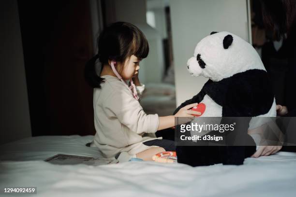 adorable little asian girl playing a doctor game with her beloved soft panda toy, listening the heartbeat of the soft panda toy with a stethoscope at home - imitación de adultos fotografías e imágenes de stock