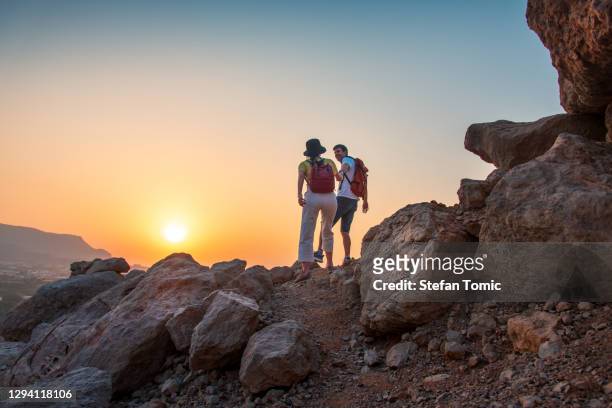 couple climbing to the mountain top in the uae desert at sunset - middle east desert stock pictures, royalty-free photos & images