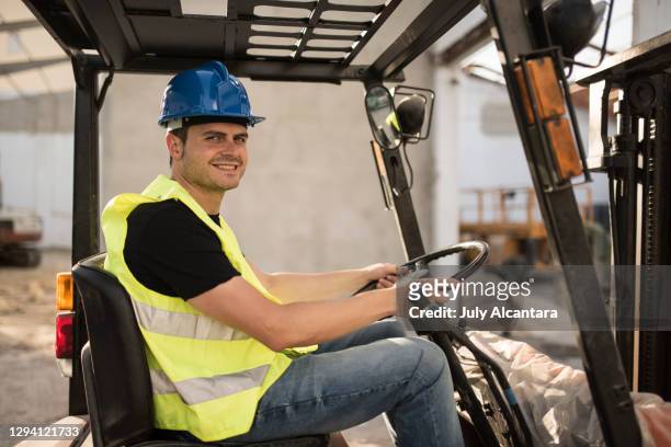 construction worker smiles and looks at camera happily during remodel work on a building. young man driving forklift - dirty construction worker stock pictures, royalty-free photos & images