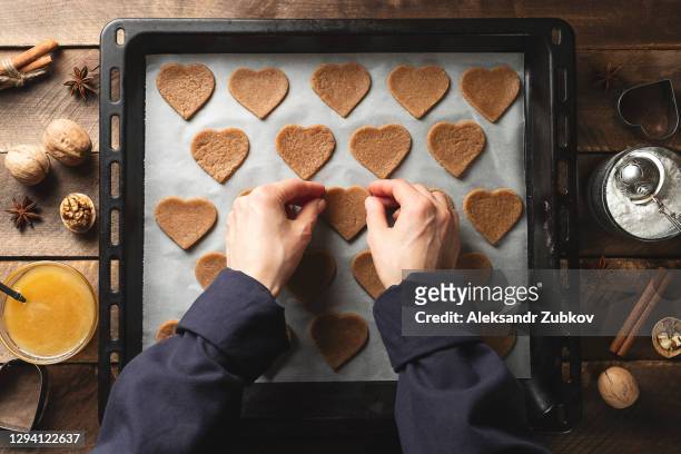 a woman, a young girl or a pastry chef lays out heart-shaped cookies on parchment baking paper, on a baking sheet, against the background of a wooden table. the concept of cooking, valentine's day. - valentine's day home stock pictures, royalty-free photos & images