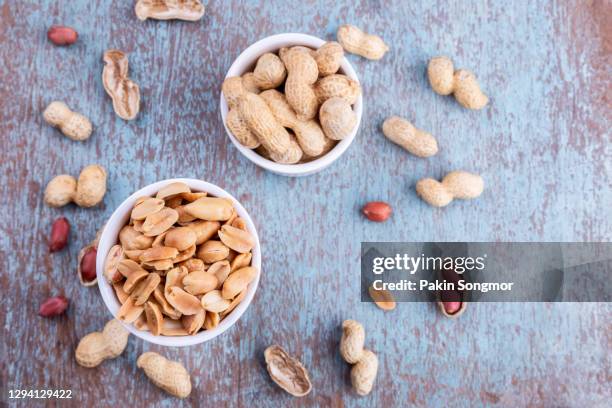 peanuts in a white bowl rests on an old wooden table. - peanuts stock pictures, royalty-free photos & images