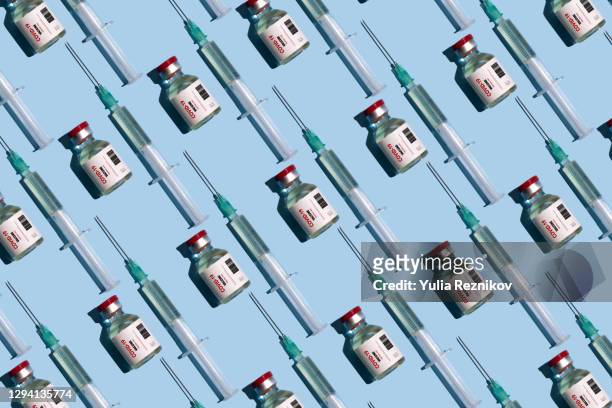 repeated vials and syringes with covid-19 vaccine on the blue background - covid 19 vaccine stock pictures, royalty-free photos & images