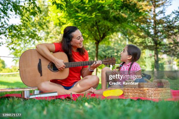 mother-daughter sitting on the grass, playing guitar, singing and having a picnic - kids picnic stock pictures, royalty-free photos & images