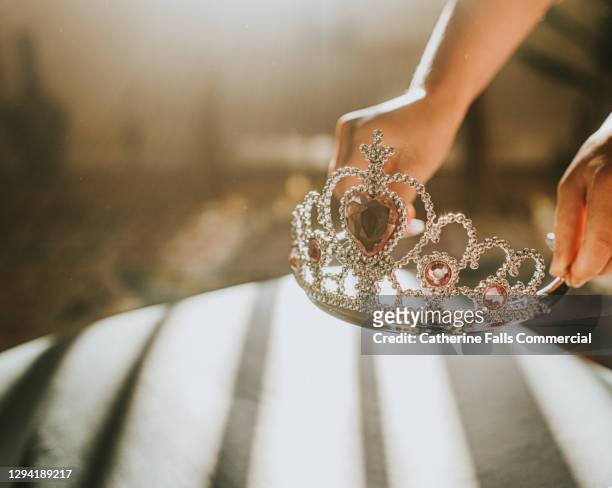 child picking up a plastic jewelled tiara toy in sunlight - königshaus stock-fotos und bilder