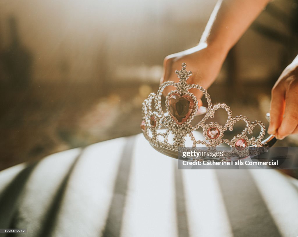 Child picking up a plastic jewelled tiara toy in sunlight