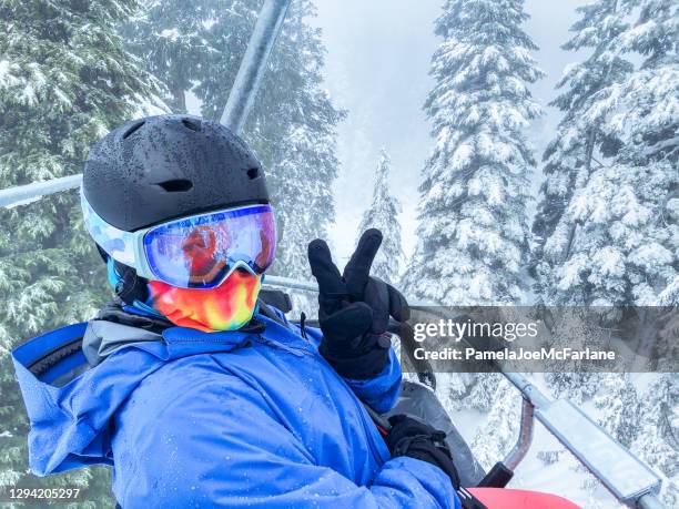 woman skier wearing helmet, goggles, neck gaiter giving peace sign - skiing helmet imagens e fotografias de stock