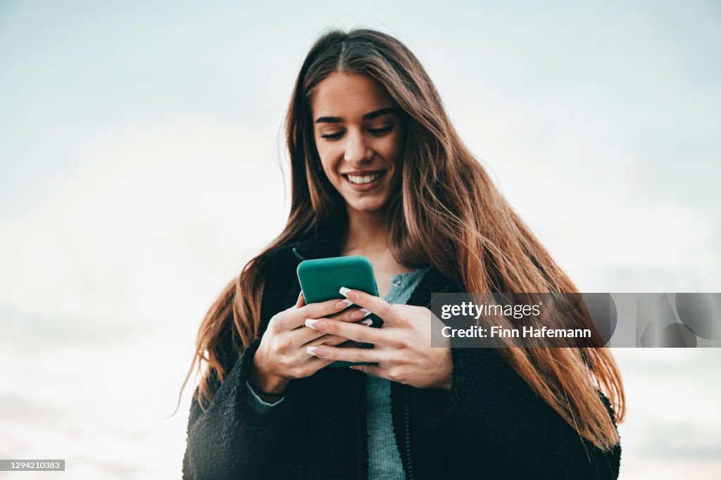 Cheerful Young Woman writing Messages on Mobile Phone