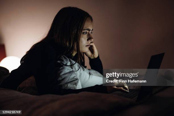 ernstige anf nadenkende jonge vrouw die berichten op laptop leest die in bed ontspant - cyberbullying stockfoto's en -beelden